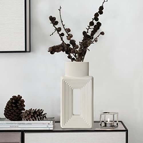 Geometric vase with dried branches on a shelf with pinecones and a small candle.